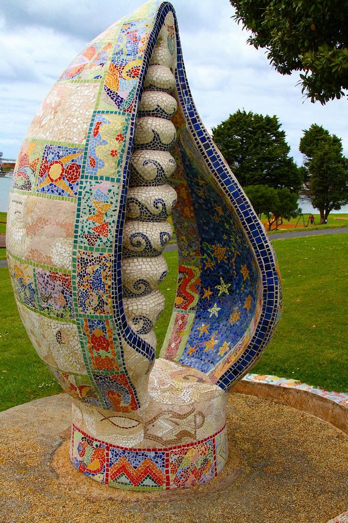 a sculpture in the shape of a shell on top of a stone slab with grass and trees behind it