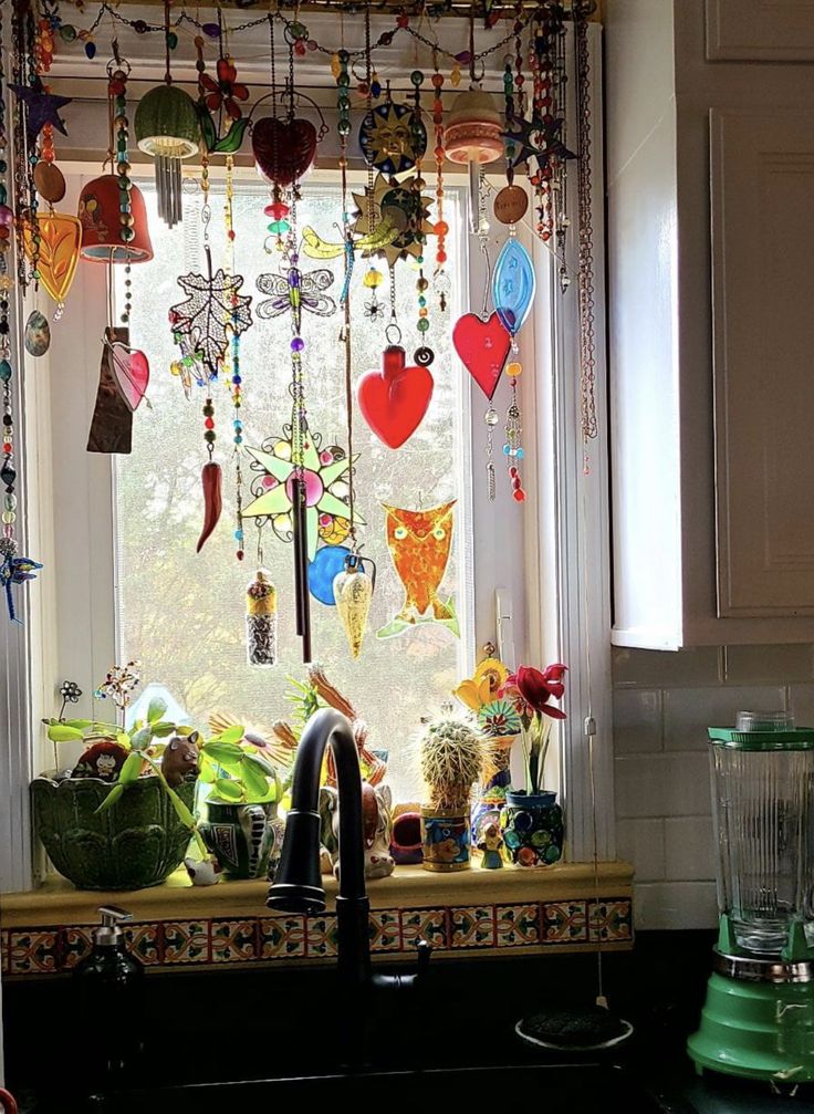 a kitchen sink under a window filled with colorful glass decorations and hanging hearts on the windowsill