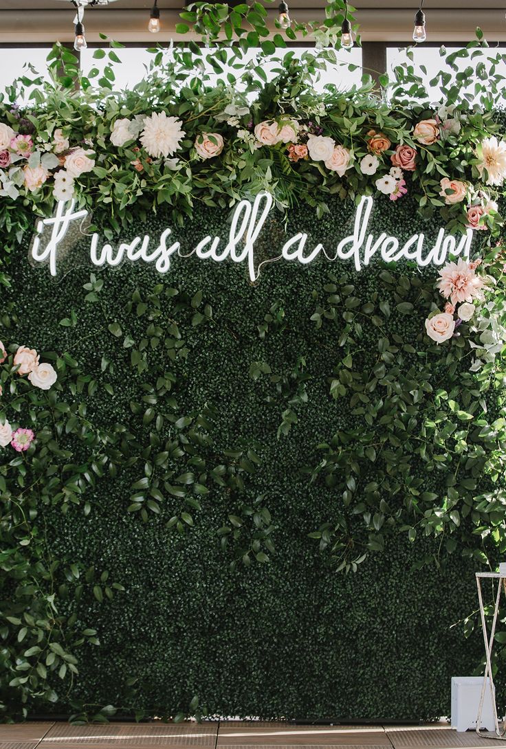 a wedding backdrop with pink flowers and greenery on the wall that says it was all a dream