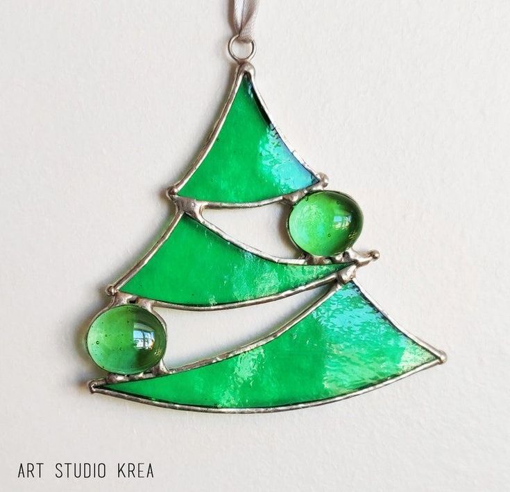 a green glass christmas tree ornament hanging from a silver plated chain on a white wall