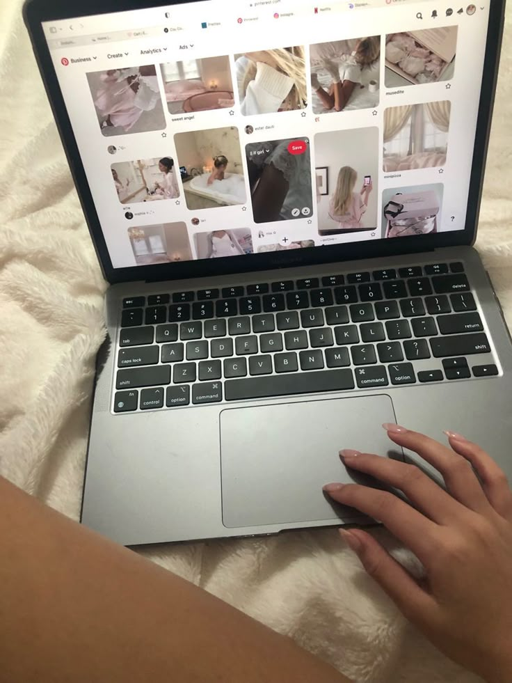 a woman is typing on her laptop while laying in bed with white sheets and pillows