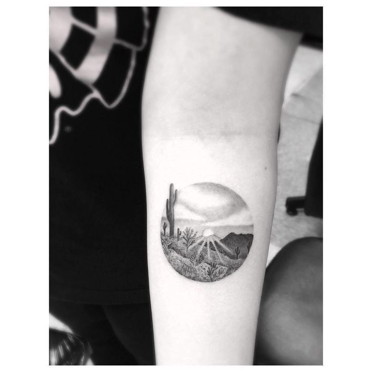 a woman's arm with a cactus and mountains tattoo on it