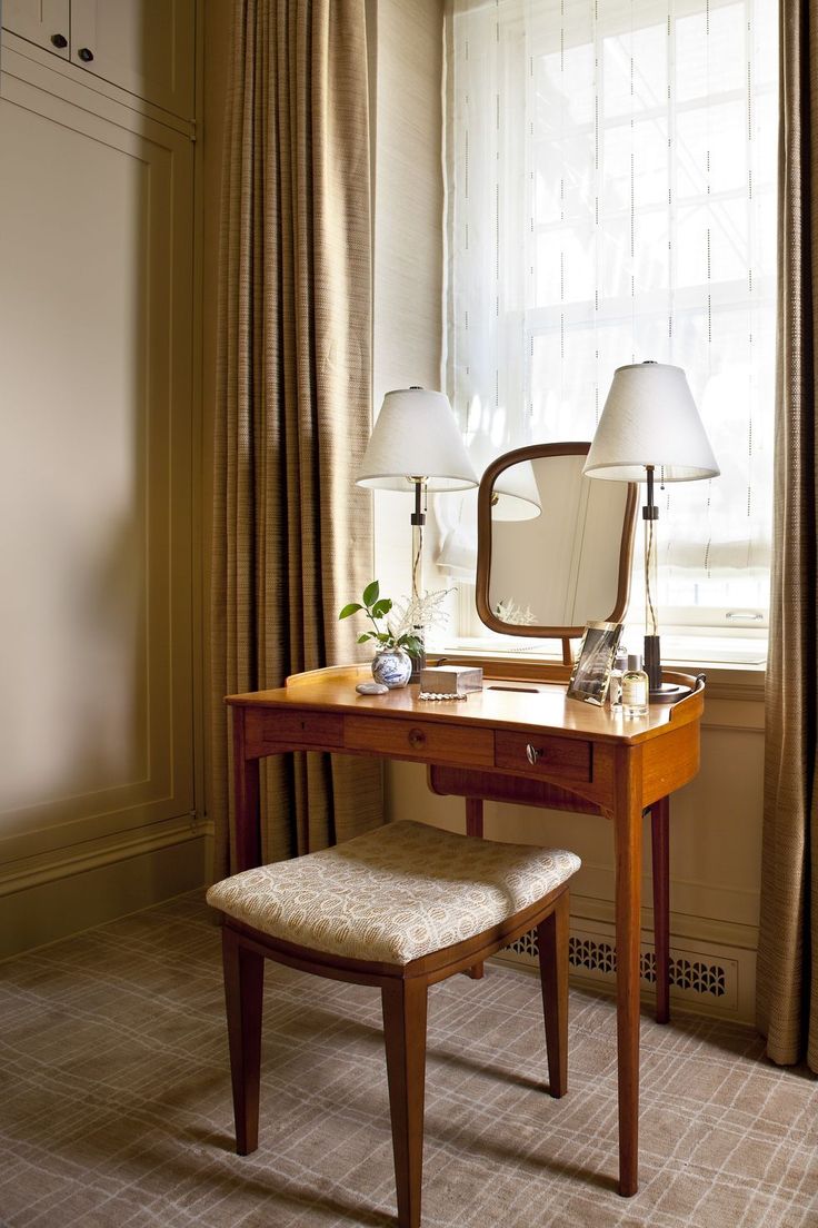 a dressing table with a mirror, stool and two lamps in front of a window