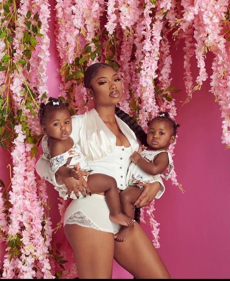 a woman holding two small children in front of pink florals on a tree branch