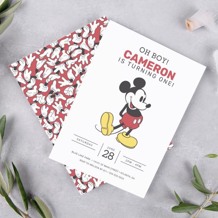 two mickey mouse birthday cards on top of a table with greenery and flowers in the background