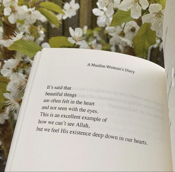 an open book sitting on top of a wooden table next to white flowers and green leaves