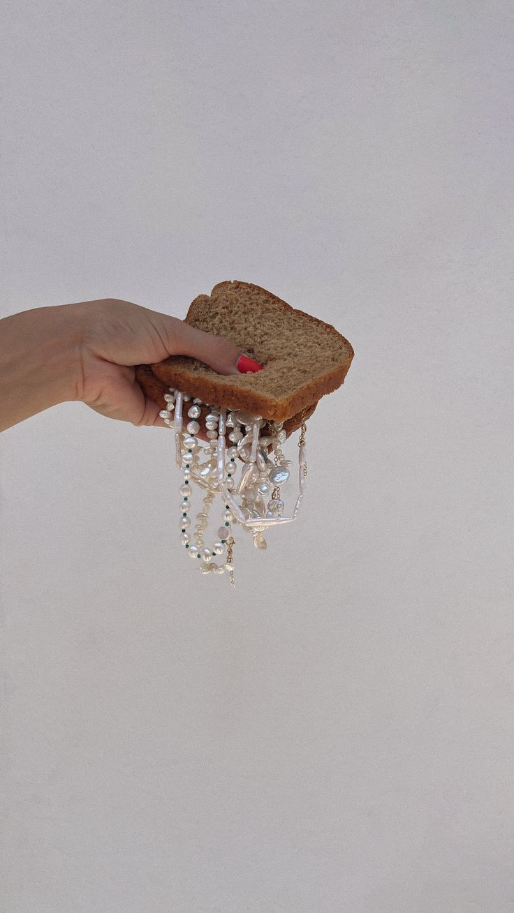 a hand holding a piece of bread with beads hanging from it