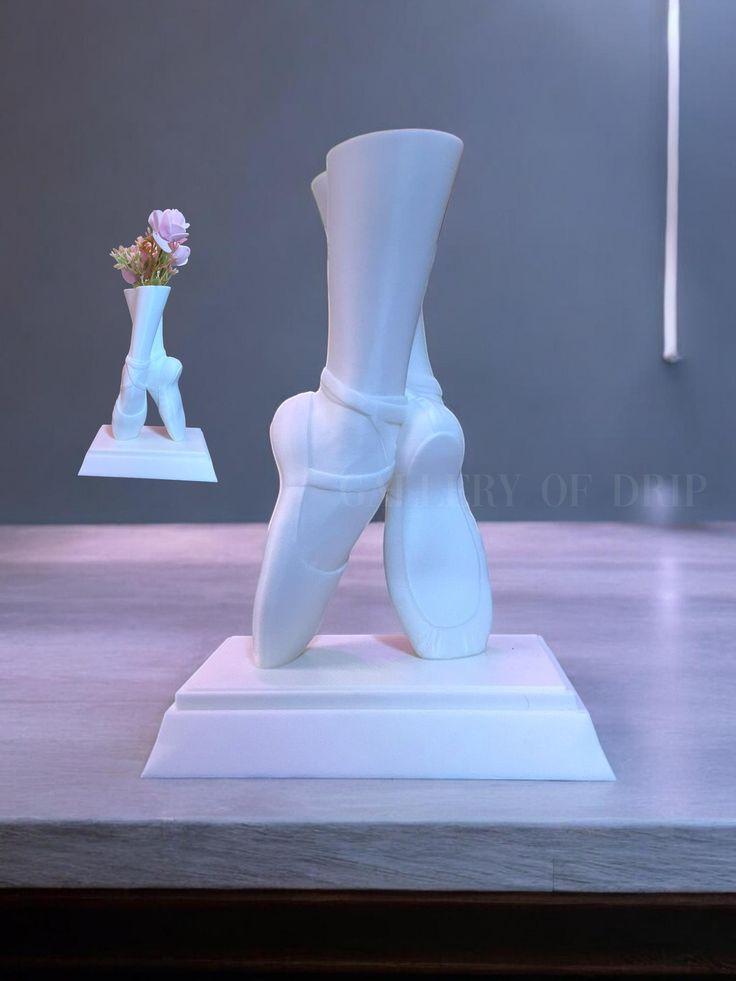 a white vase with a flower in it next to a pair of shoes on a table