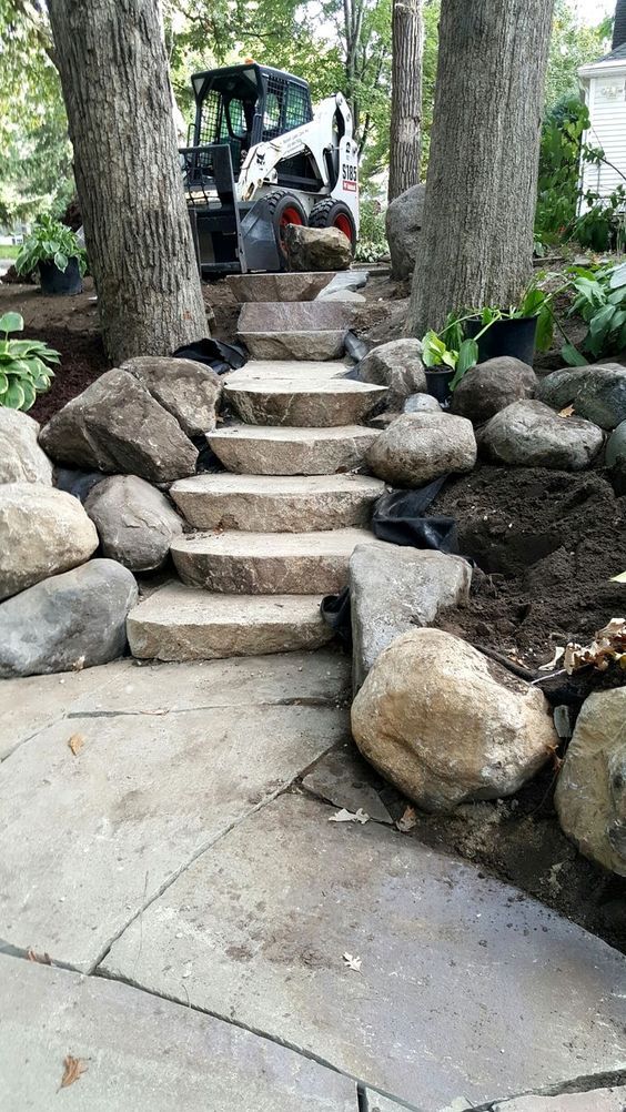 a stone path with steps leading up to a tractor parked in the back yard next to some trees