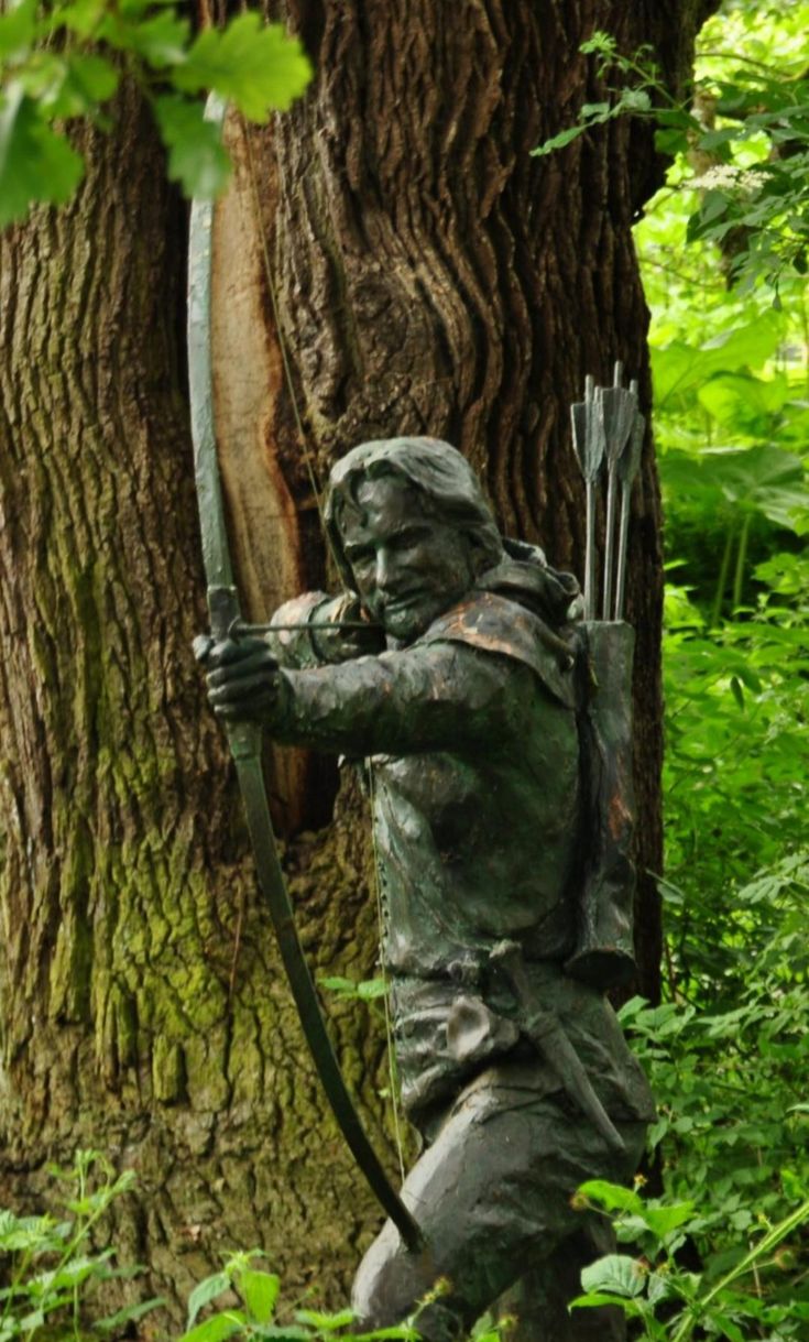 a statue of a man with a bow and arrow in the woods near a tree