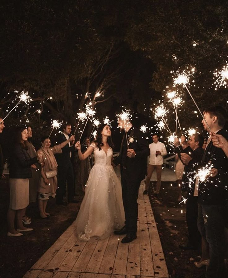 a bride and groom walking down a path holding sparklers