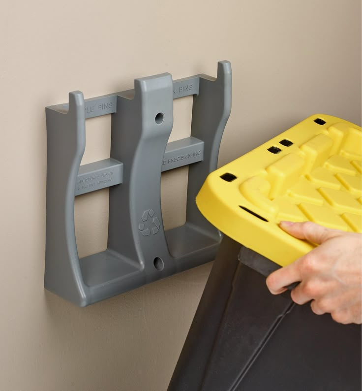 a person holding a yellow plastic object in their hand next to a wall mounted shelf