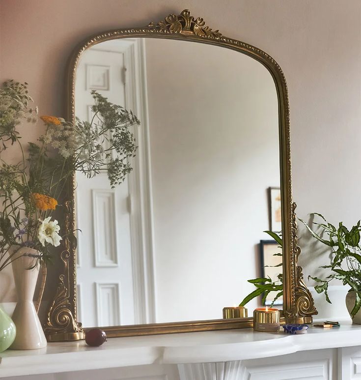 a mirror sitting on top of a mantle next to a vase with flowers in it