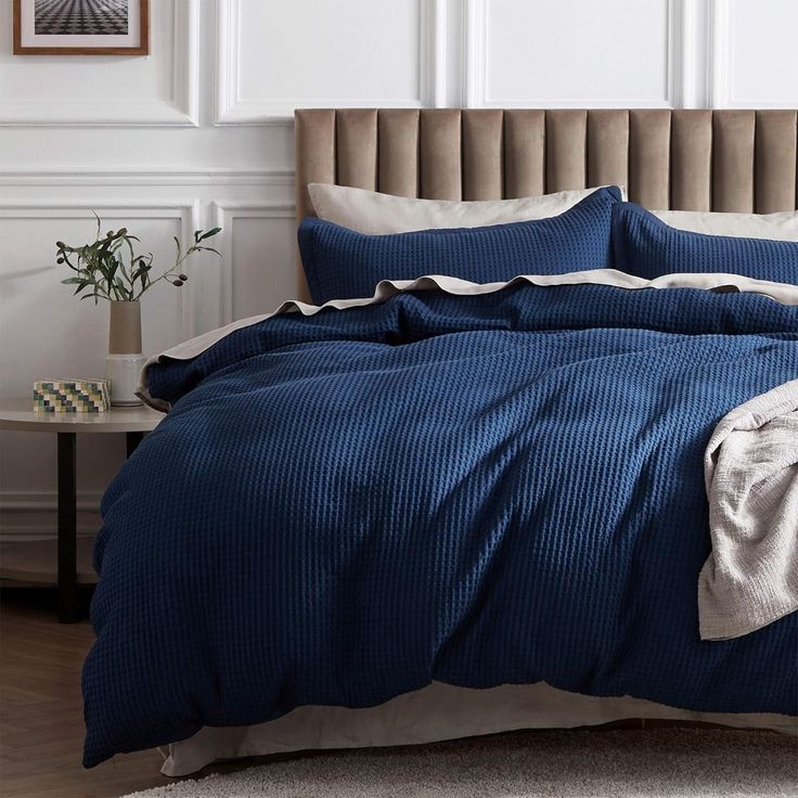 a bed with blue comforter and pillows in a white room next to a table