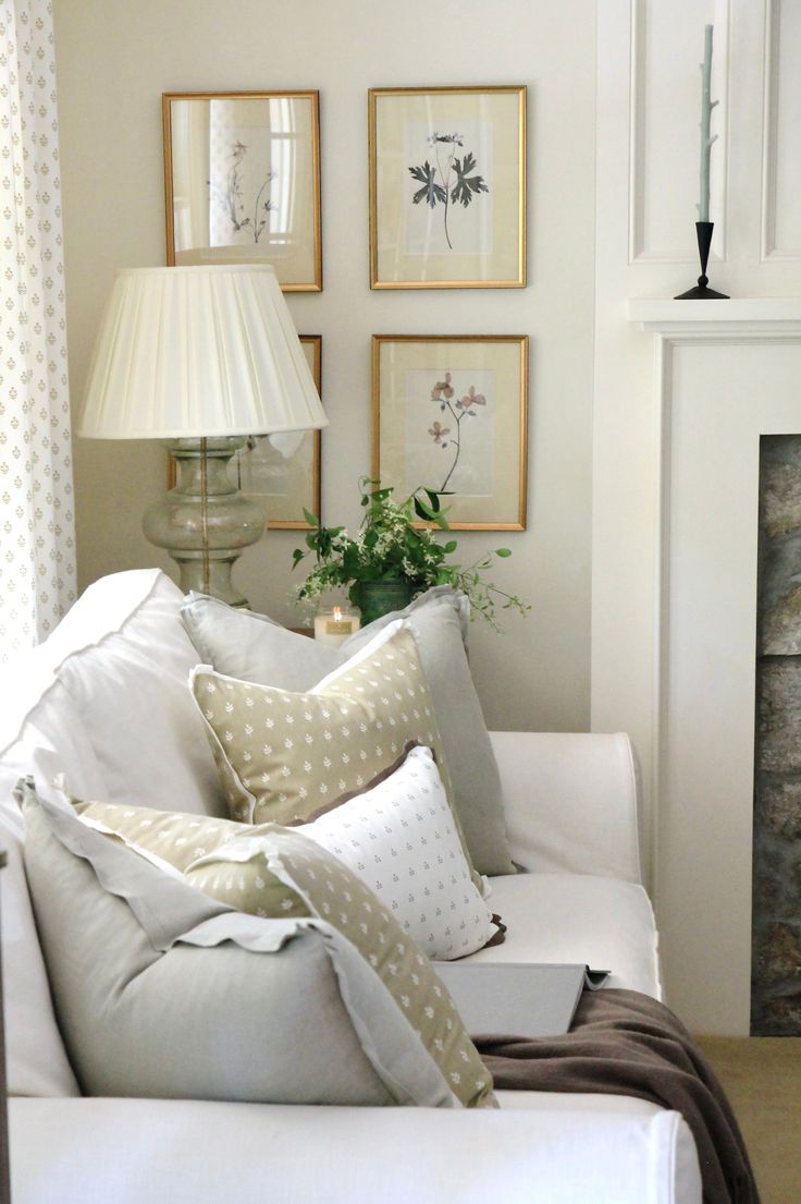 a living room filled with white furniture and pictures on the wall above it's fireplace