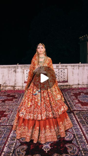 a woman in an orange and red dress standing on top of a rug with her hands behind her back