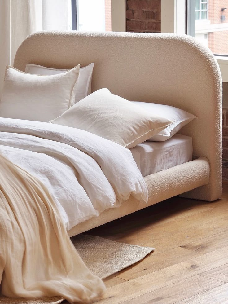 an unmade bed with white linens and pillows on top of it in front of a window