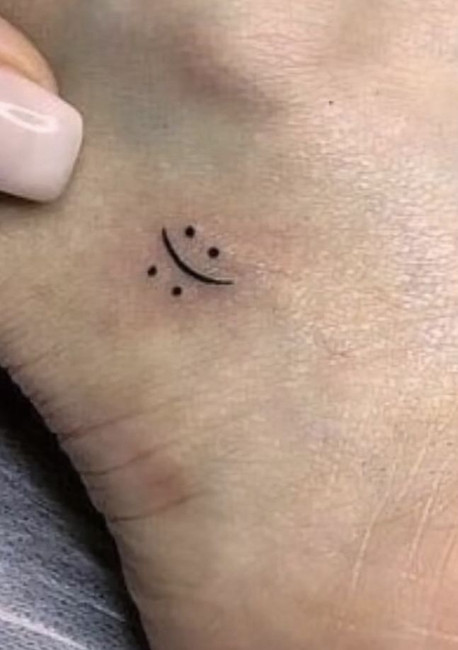 a small smiley face tattoo on the left side of the wrist is shown in black ink