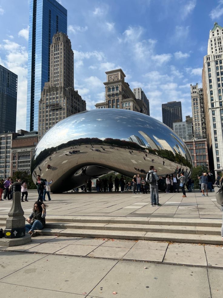 people are sitting on steps in front of a large shiny object