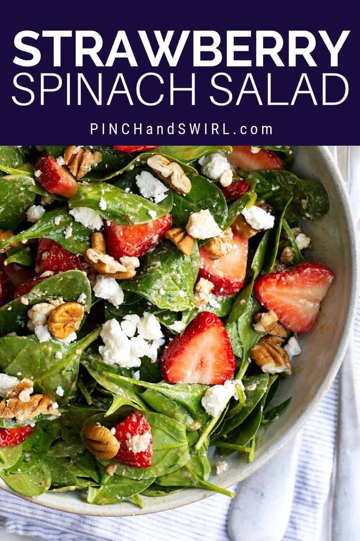 spinach salad with strawberries and feta cheese in a white bowl on a blue towel