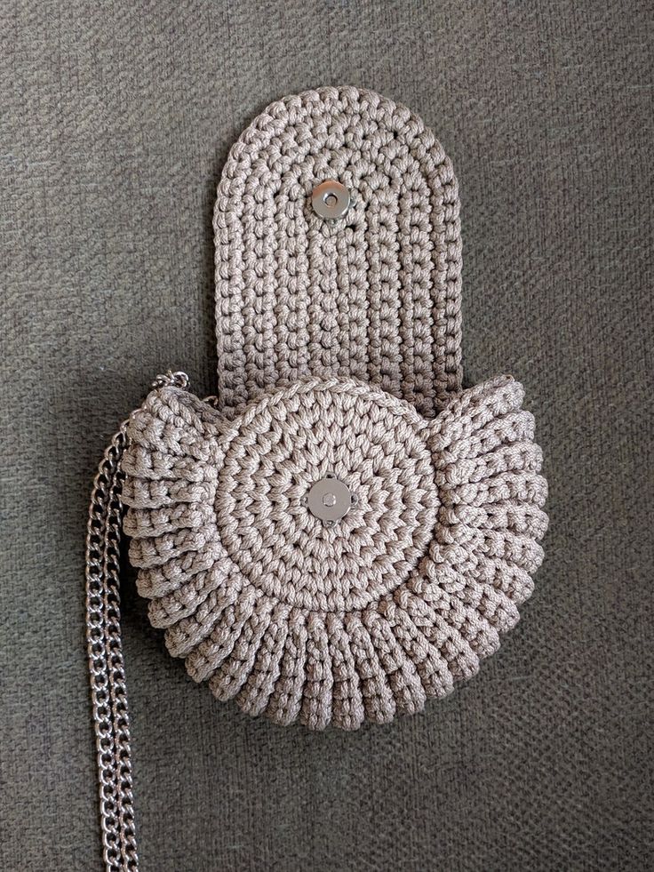 a crocheted purse sitting on top of a gray surface next to a chain