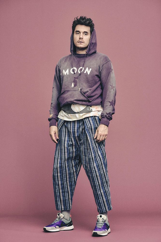 a young man is standing in front of a pink background wearing a purple hoodie and striped pants