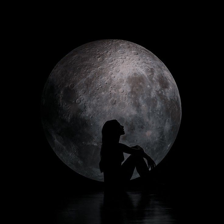 a woman sitting on the ground in front of a full moon