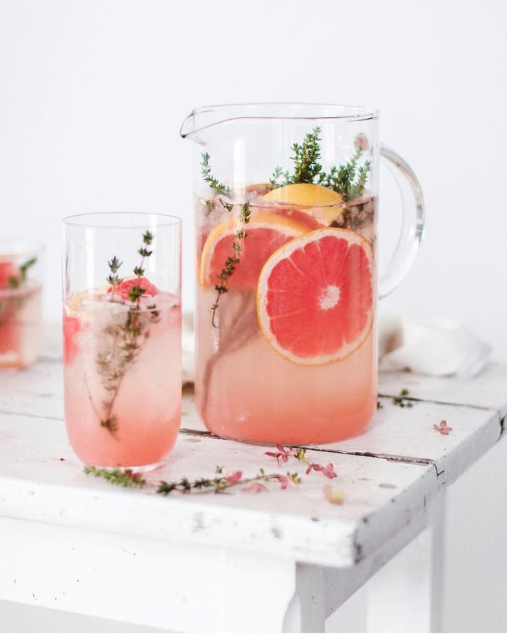 a pitcher filled with pink lemonade and garnish next to two glasses full of water