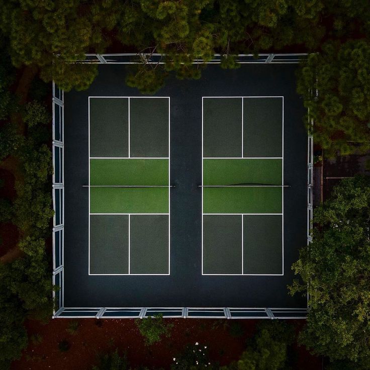 an aerial view of two tennis courts surrounded by trees