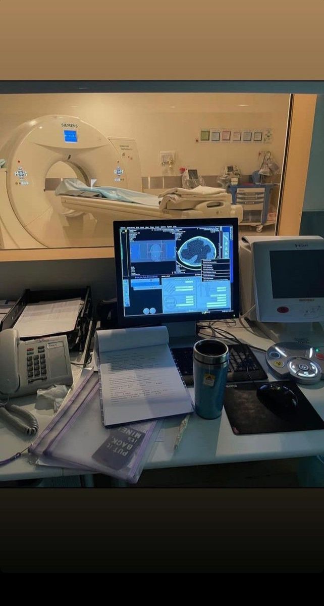 a desk with a laptop, monitor and other items on it in front of a mri room