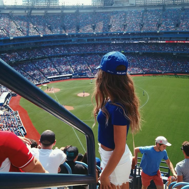 a girl in a blue hat stands at the top of a baseball field as people watch from the bleachers