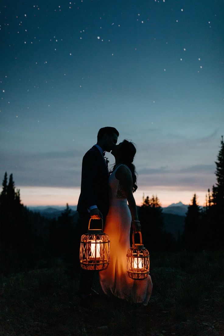 a bride and groom kissing in front of the night sky with their lanterns lit up