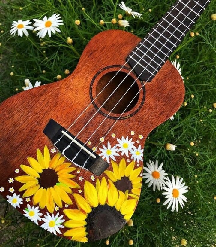 an ukulele with sunflowers and daisies painted on it sitting in the grass