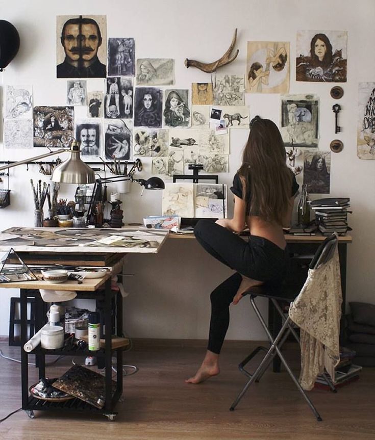 a woman sitting at a desk in front of a wall covered with pictures