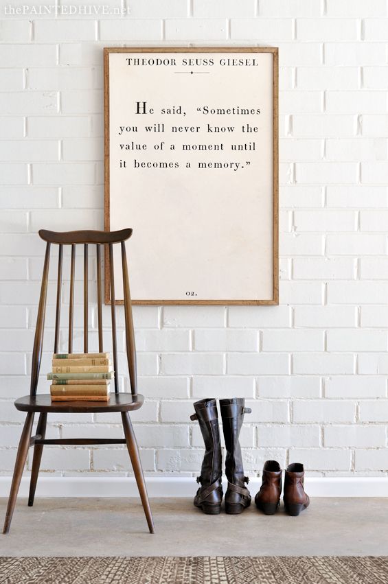 a wooden chair sitting in front of a white brick wall with a poem on it