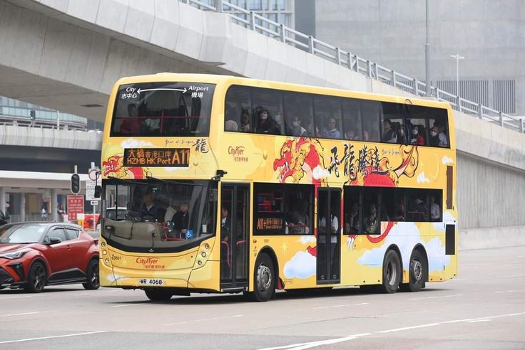 a yellow double decker bus driving down a street next to a red car and bridge