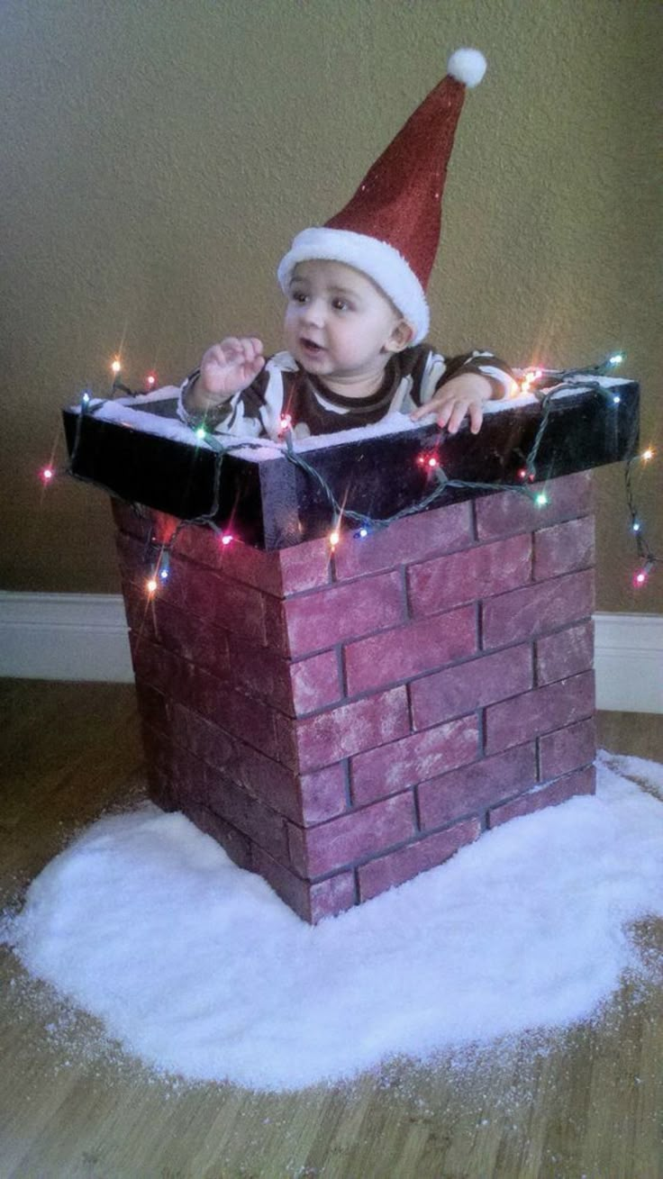 a baby wearing a santa hat sitting on top of a brick chimney with christmas lights