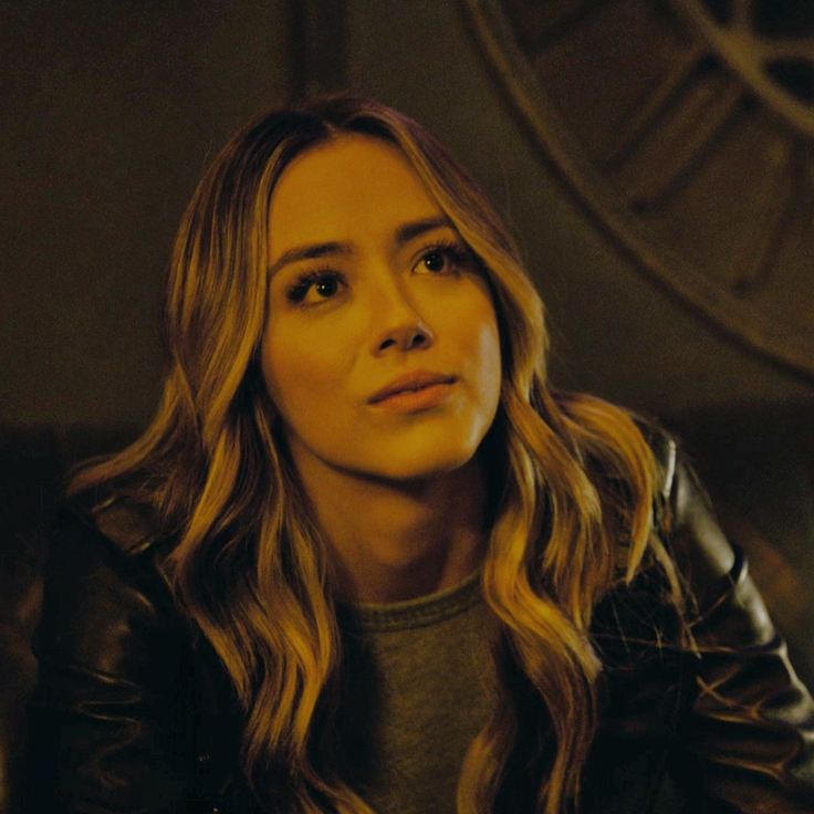 a woman with long blonde hair sitting in front of a clock