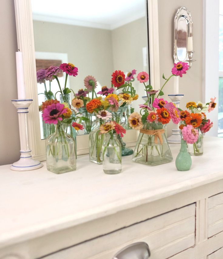 several vases filled with colorful flowers sit on a counter in front of a mirror