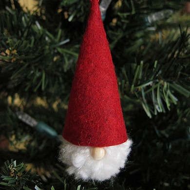 a red and white christmas ornament hanging from a pine tree in the shape of a santa's hat