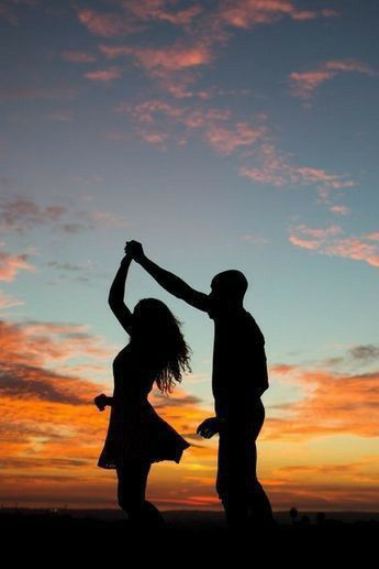 the silhouette of two people dancing in front of an orange and blue sky at sunset