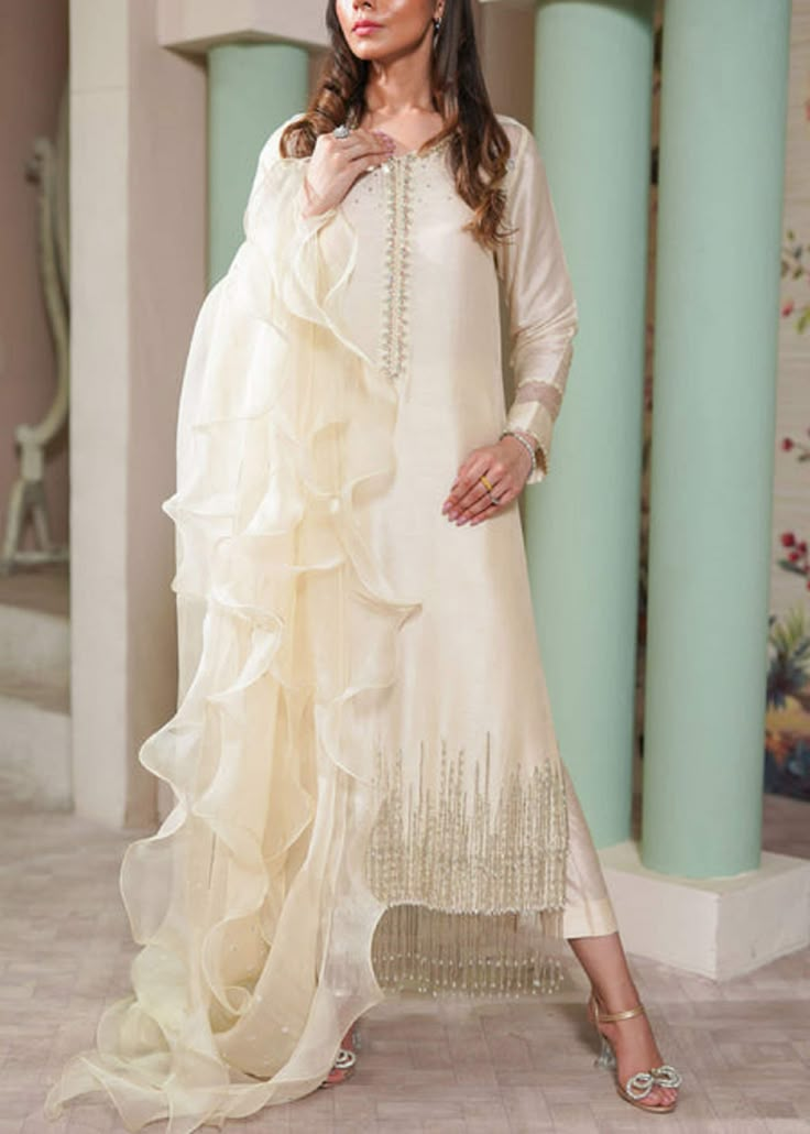 Luxurious Upada Silk: Indulge in luxury with our upada silk kurta set, offering a rich and opulent texture that exudes sophistication. Exquisite Hand Embroidery: Adorned with intricate hand embroidery, the kurta features delicate detailing that adds a touch of timeless elegance. Pearl and Beads Embellishments: Experience a blend of tradition and glamour with the pearl and bead embellishments, beautifully hanging over the hemline for a graceful finish. Coordinated Pants: The set includes perfectly coordinated pants, providing a stylish and comfortable bottom that complements the ornate kurta. Graceful Organza Ruffle Dupatta: Elevate your look with the ethereal beauty of the organza ruffle dupatta, adding a layer of grace and charm to the ensemble. Versatile Statement Piece: Ideal for specia White Raw Silk Dress Pakistani, Luxury Elegant Dupatta With Intricate Design, Luxury Sheer Nida Dupatta, Raw Silk Suits Designs, Luxury Tissue Silk Dupatta For Party, Luxury Party Sets For Eid, Luxury Cream Tissue Silk Dupatta, Party Traditional Wear With Pearl Embroidery, Festive Sharara With Pearl Embroidery And Traditional Drape