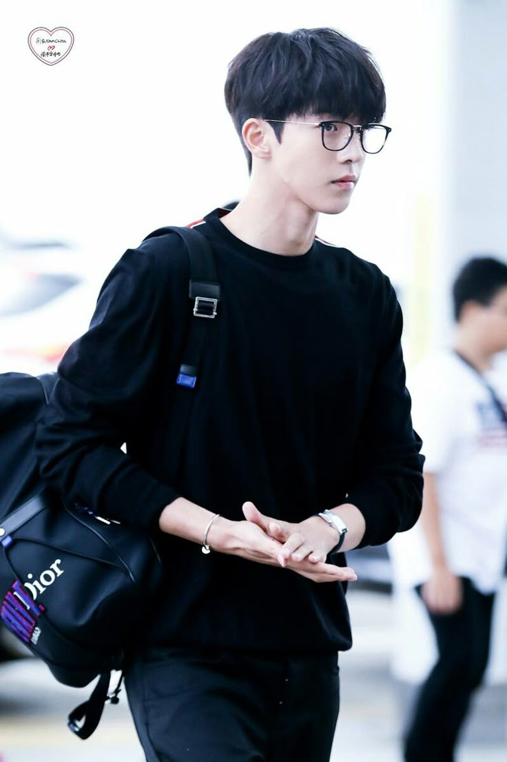 a young man wearing glasses and carrying a black bag