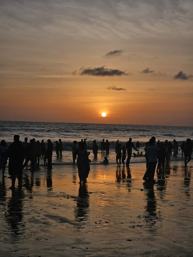 a group of people standing on top of a beach next to the ocean at sunset