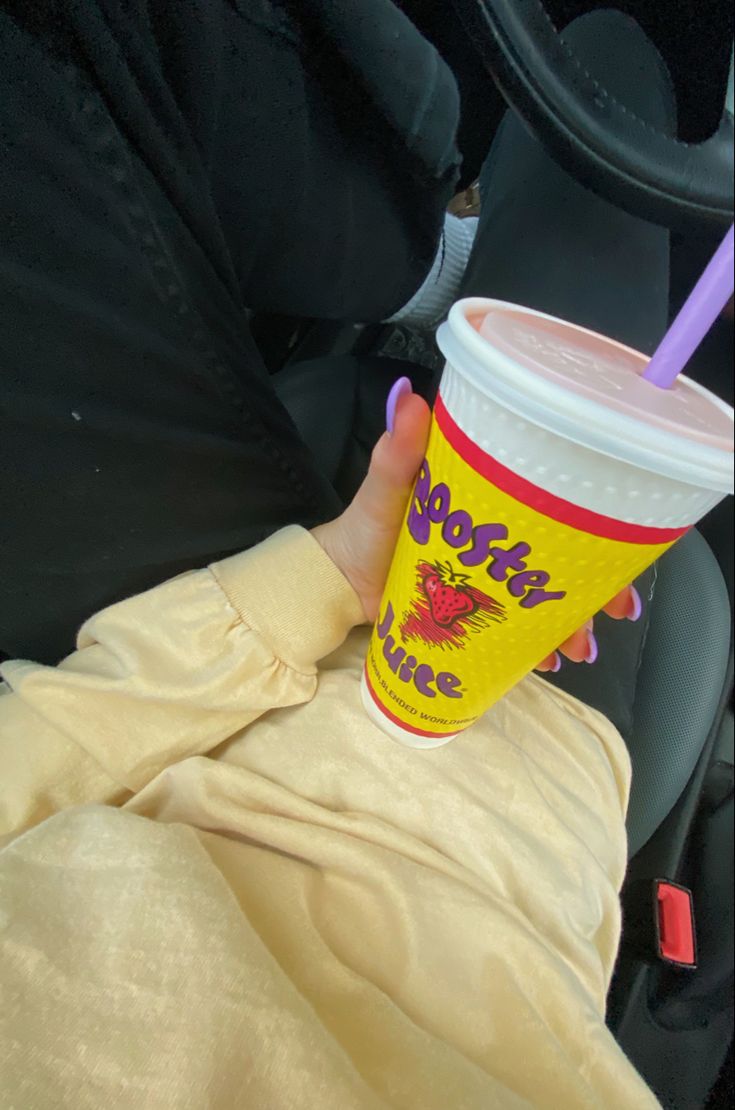 a person holding up a cup with a straw in it's hand while sitting in the back seat of a car