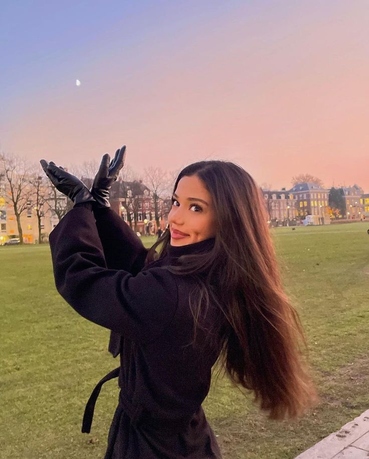 a woman with long hair and black gloves is posing for the camera in a park