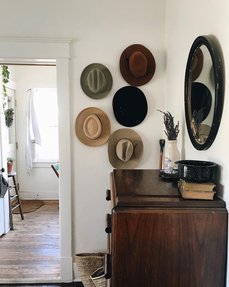 hats are hanging on the wall above a dresser in a room with wood floors and white walls