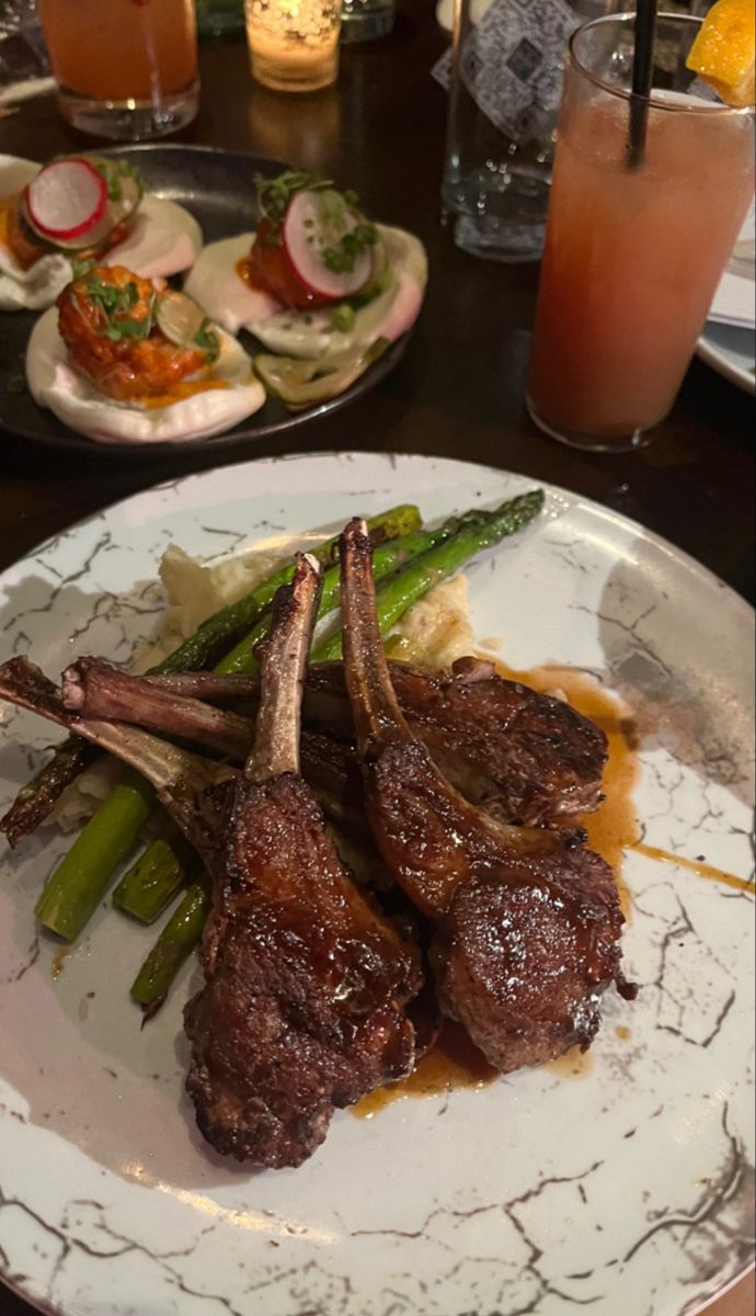 a plate with some meat and vegetables on it next to glasses of orange juice in the background