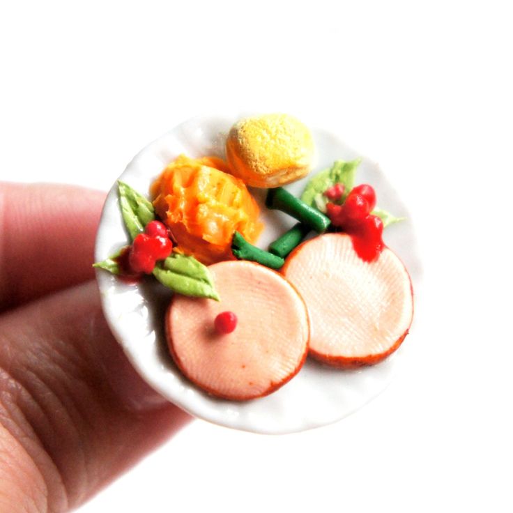 a hand holding a miniature white plate with food on it's side and two small pieces of fruit in the middle