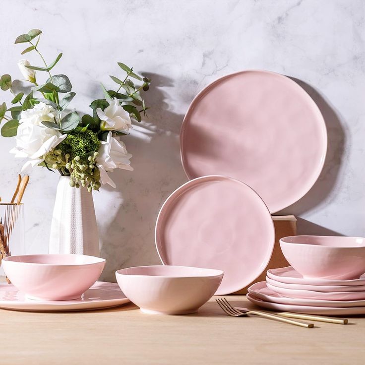 pink dinnerware set on wooden table with flowers in vase